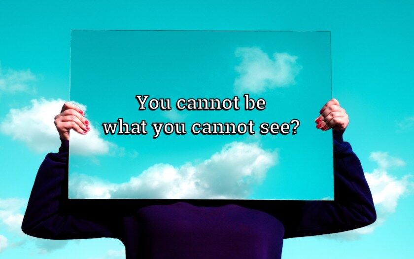 A person holds up a large mirror, covering their face and only showing their arms. Behind them and also reflecting in the mirror, a bright blue sky with several clouds are visible. The image is subtitled, "You cannot be what you cannot see?"